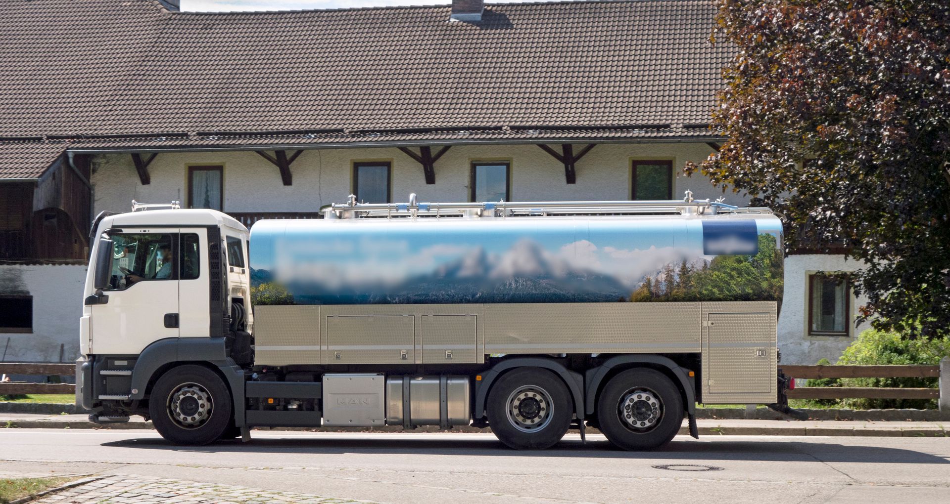 Water tanker truck parked in front of a house. The tank has a landscape mural.