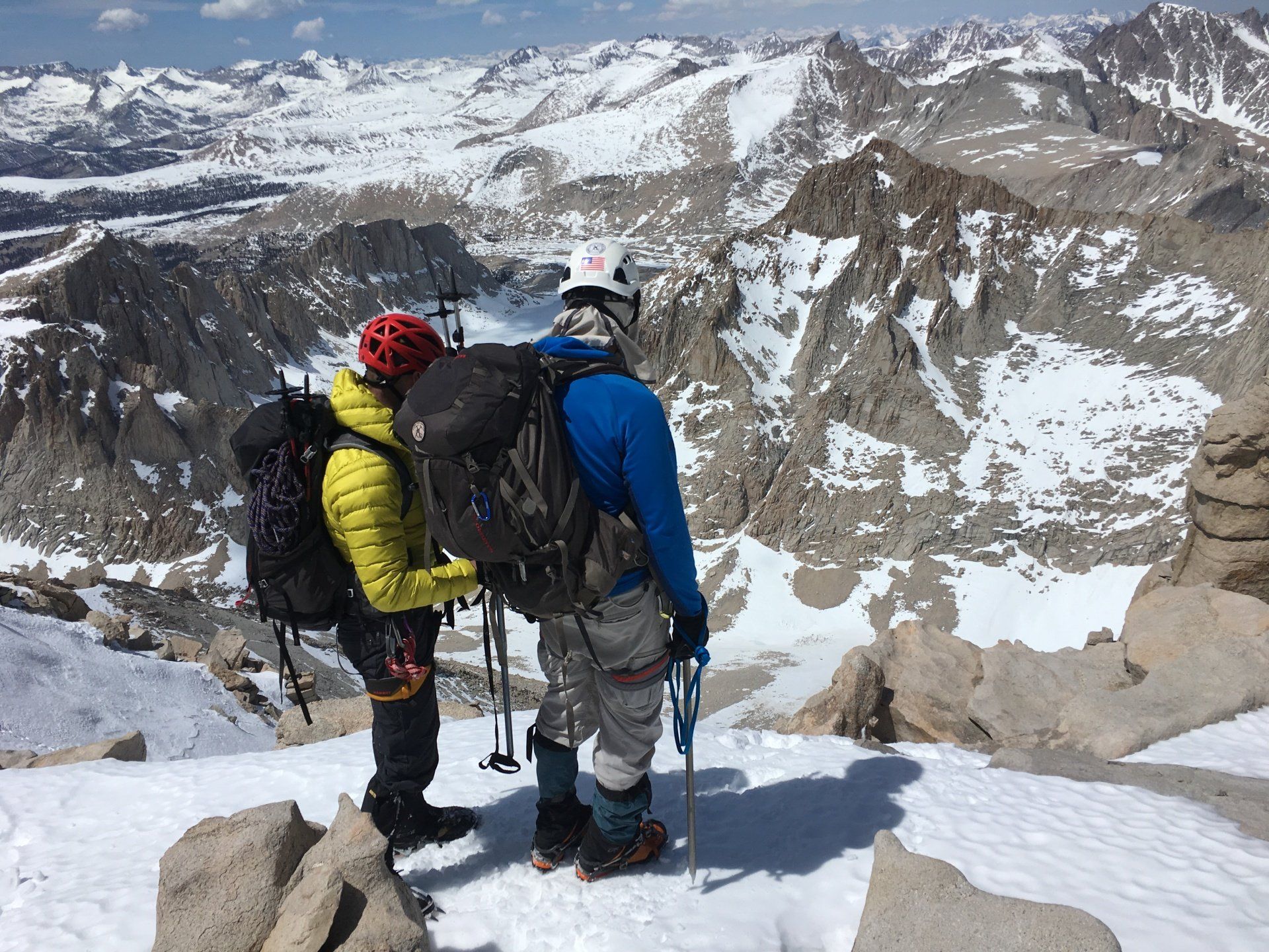Two climbers on a snowy mountain summit, overlooking a vast, snowy landscape.