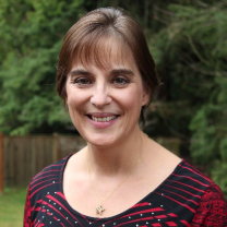 Jennifer with short brown hair smiles, wearing a red and black patterned top; outdoor setting.