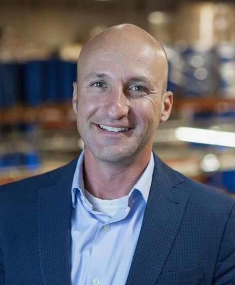 Pete Stamper smiles, wearing a blue blazer and light blue shirt, in a warehouse setting.