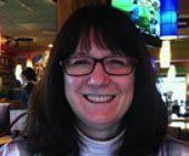Sandy King with dark hair, glasses, smiling in a restaurant setting.