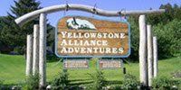 Sign for Yellowstone Alliance Adventures, wooden posts with a wooden sign, green grass background.