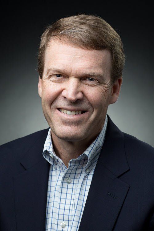 Bob King with brown hair, smiling, wearing a blue blazer over a checkered button-down shirt.