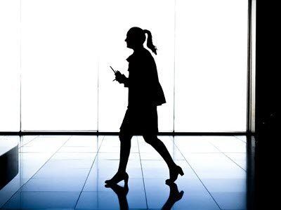 Silhouette of person walking, holding phone, in modern hallway with bright background.