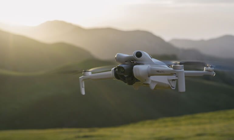 Dron blanco en vuelo contra un cielo azul brillante, con las hélices girando.