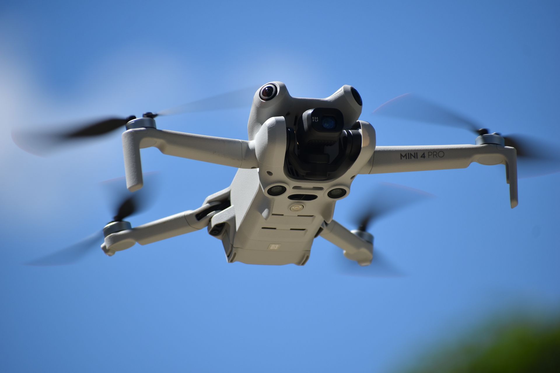 Dron blanco en vuelo contra un cielo azul brillante, con las hélices girando.