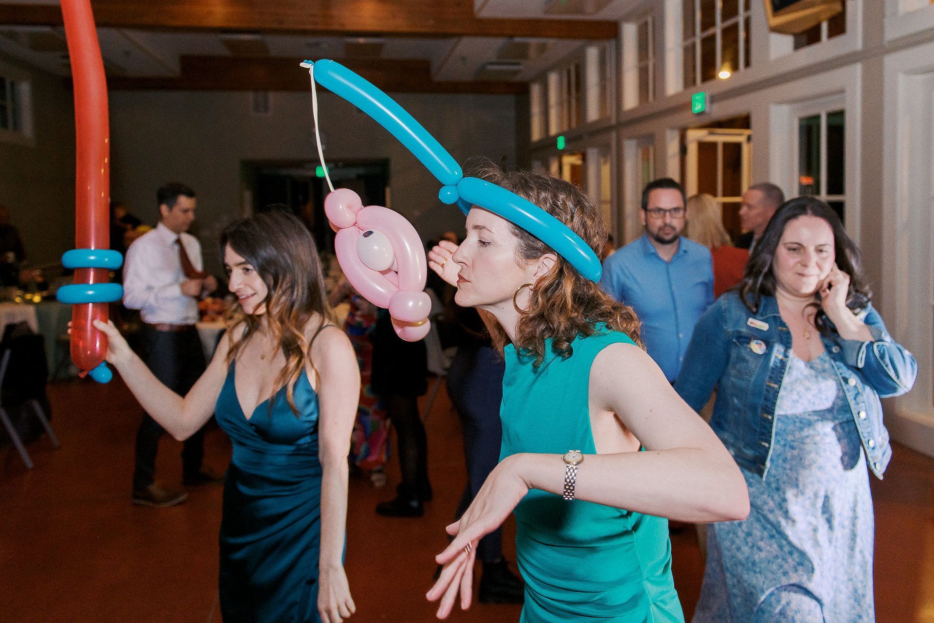 A group of people are dancing at a party with balloons on their heads.