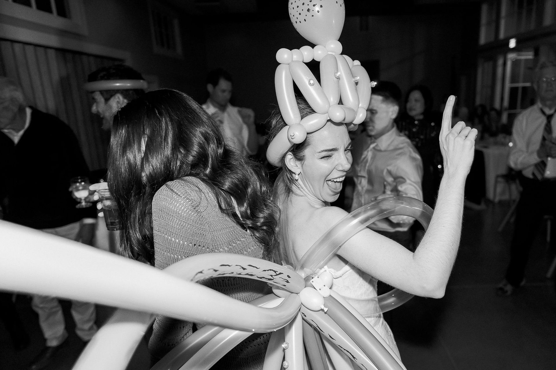 A woman in a wedding dress is dancing with balloons on her head.