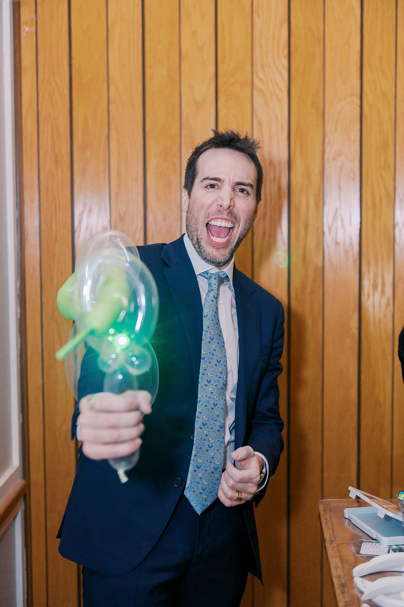 A man in a suit and tie is holding a green balloon.