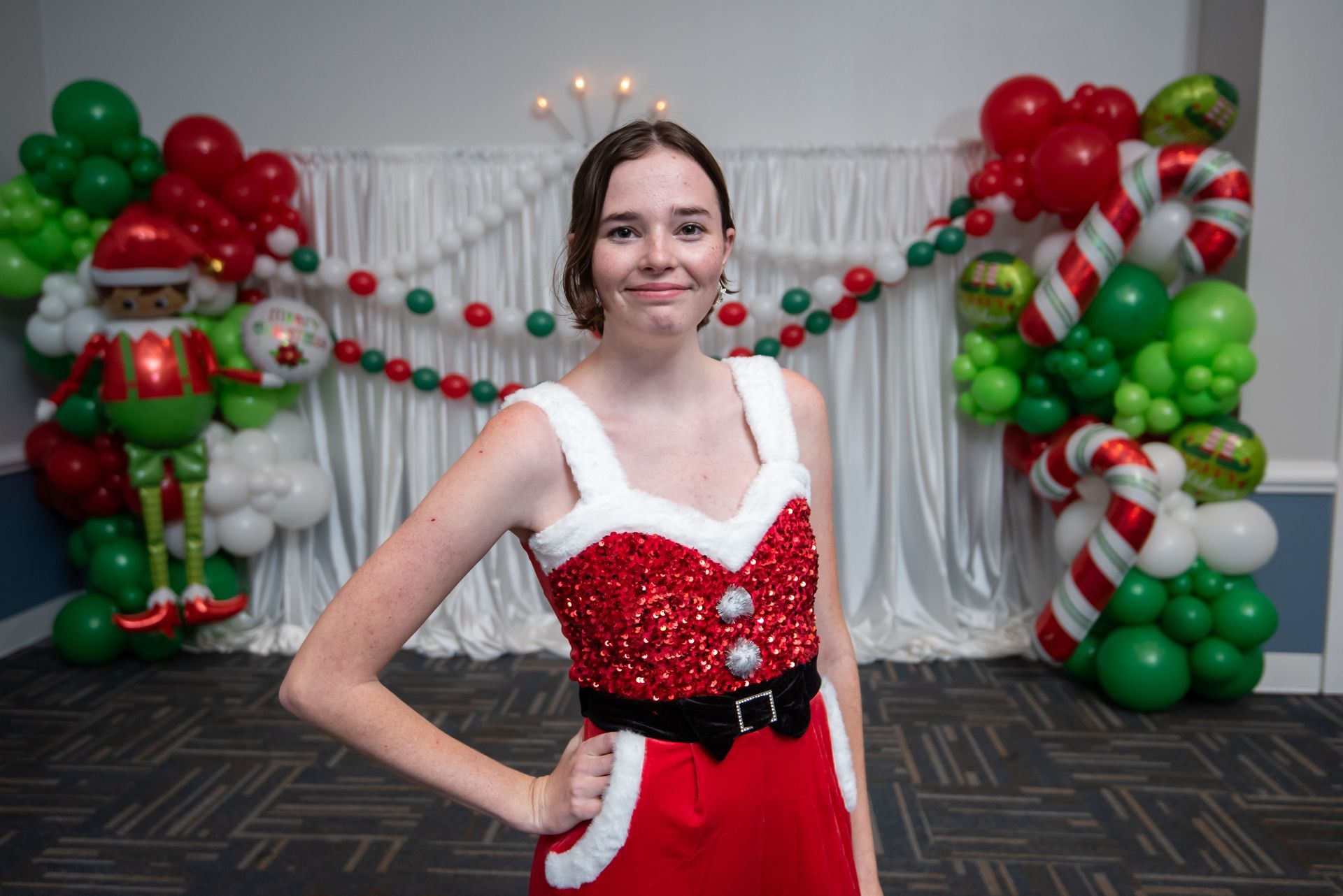 A woman in a santa claus costume is standing in front of a christmas decoration.