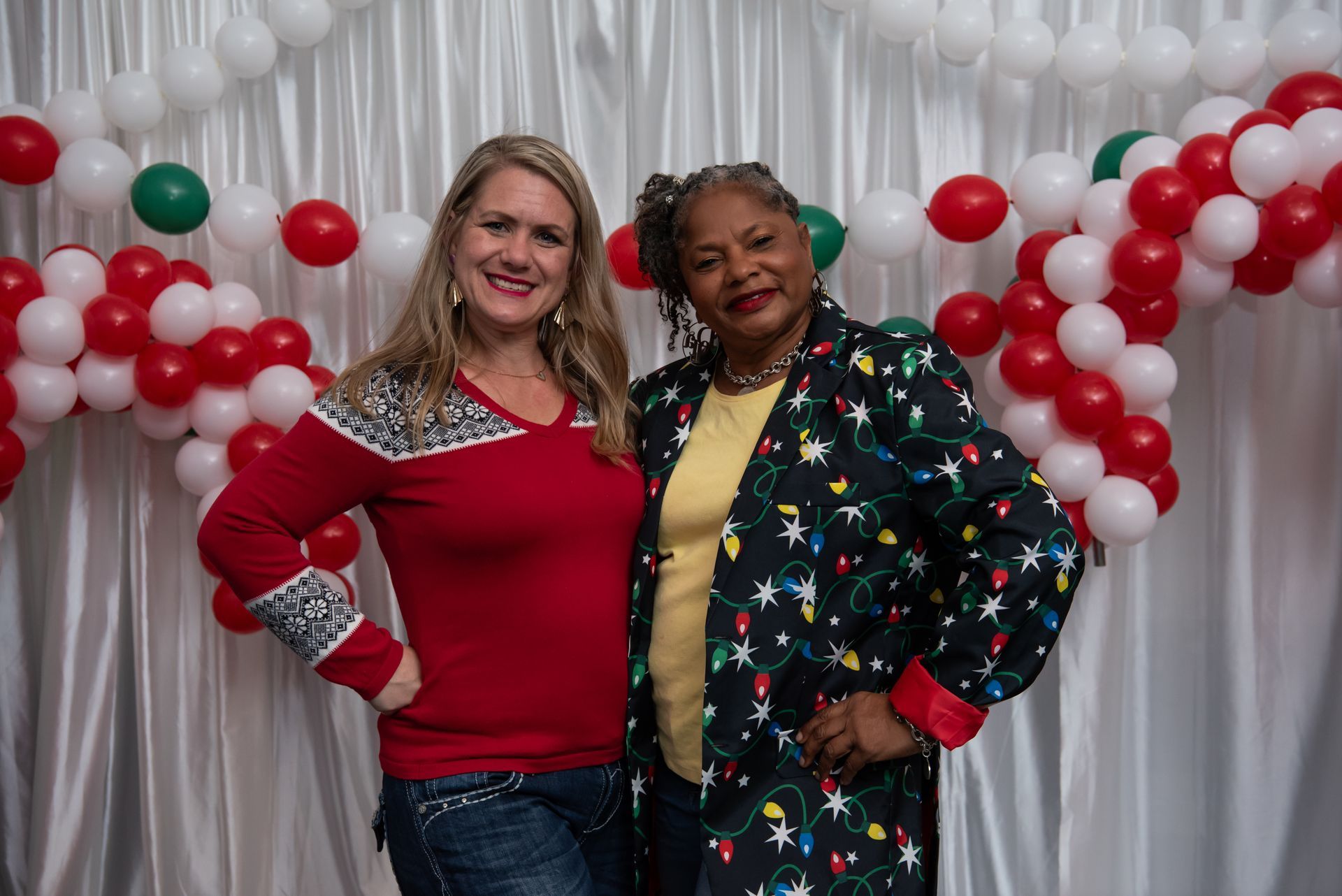 Two women are posing for a picture in front of balloons.