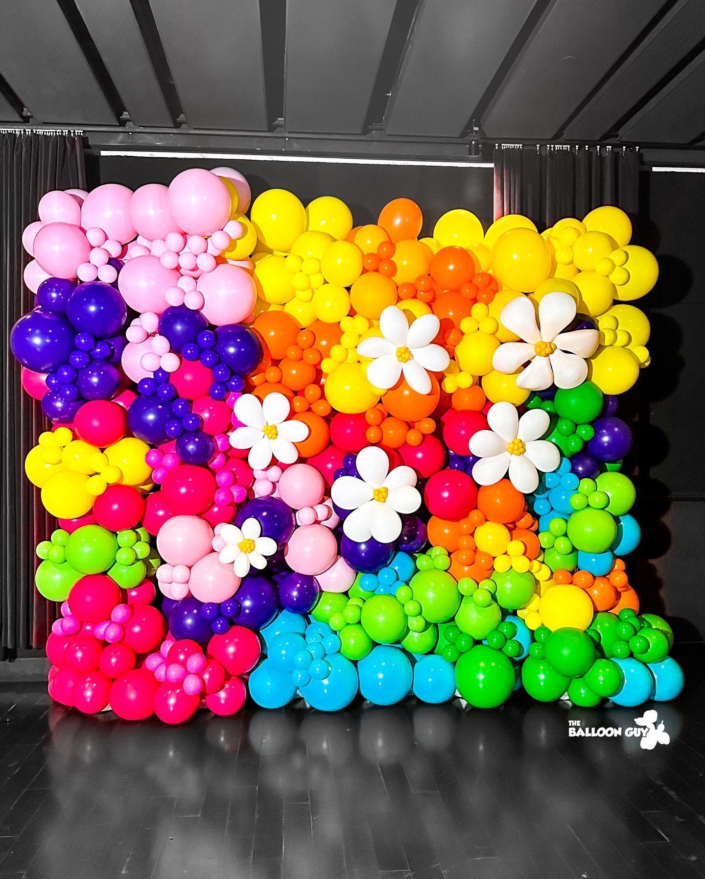 A wall of colorful balloons with flowers on them