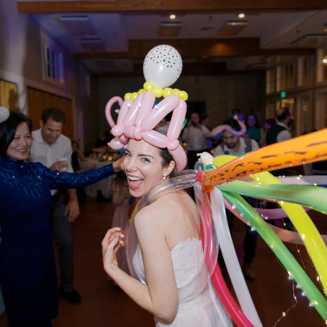 A woman in a white dress is wearing a hat made of balloons and ribbons