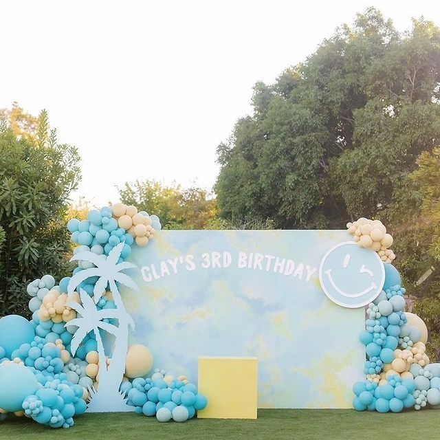 A wall decorated with balloons and palm trees for clay 's 3rd birthday