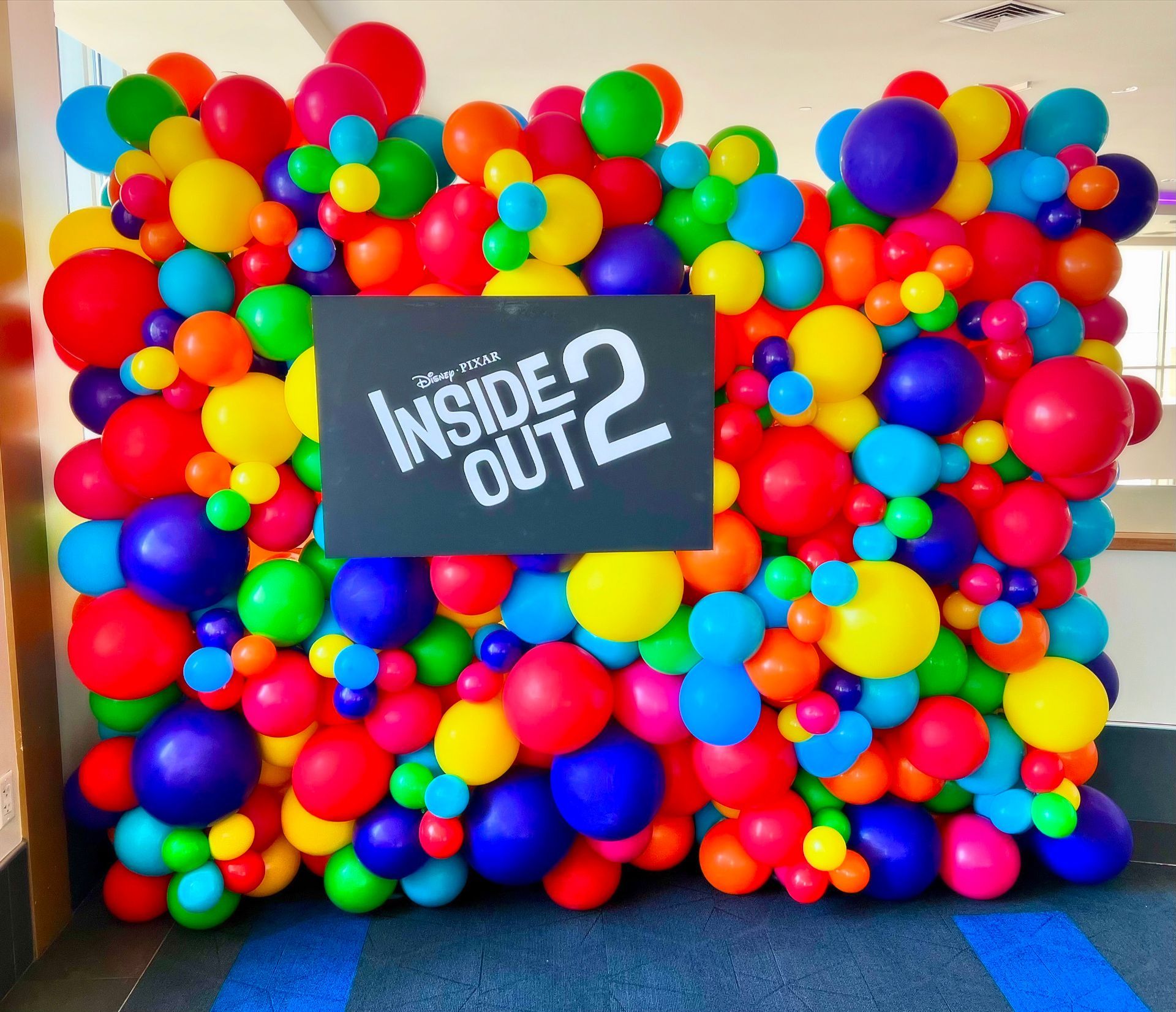 A wall of colorful balloons with a sign that says inside out 2