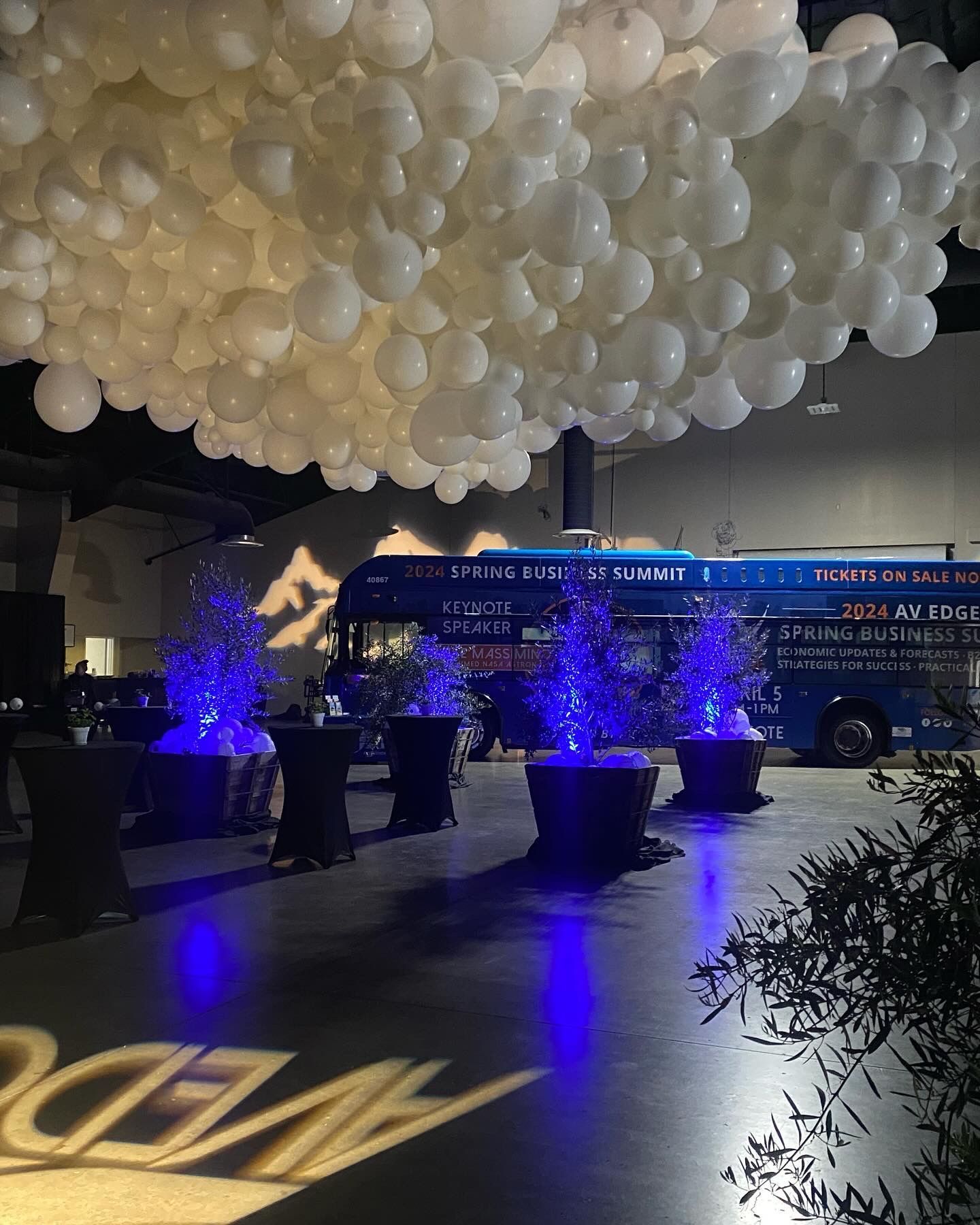 A blue bus is parked under a cloud of white balloons