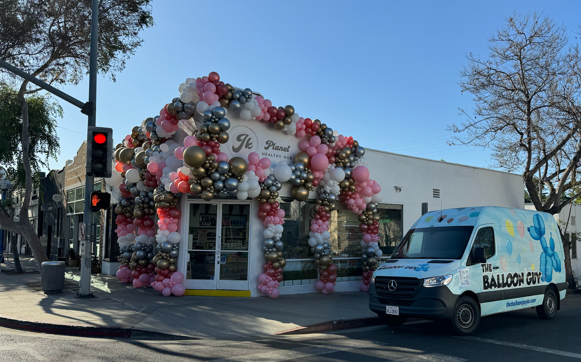 A white van is parked in front of a building decorated with balloons.