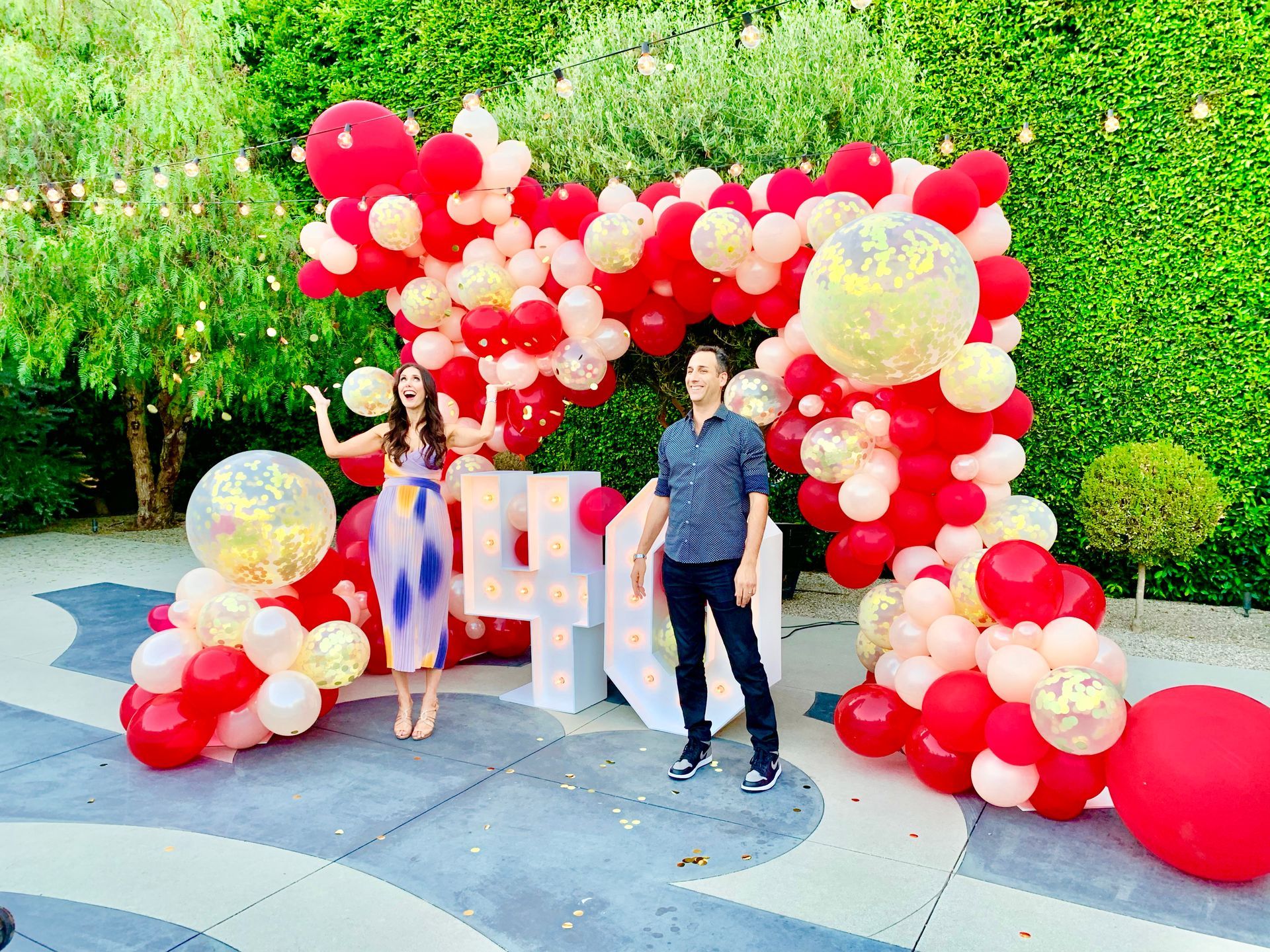 A man and a woman are standing in front of a balloon arch.