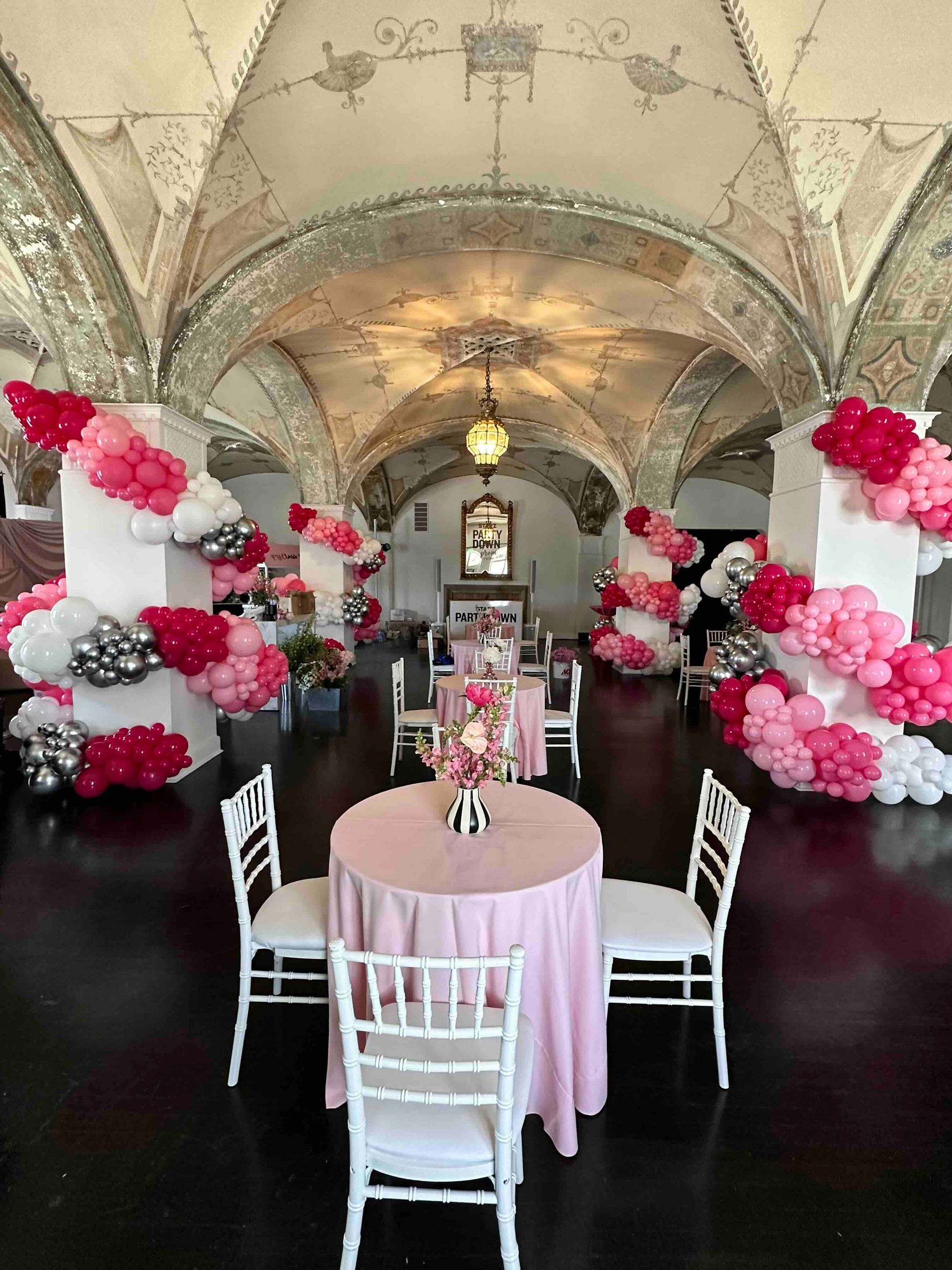 A room filled with tables and chairs decorated with pink and white balloons.