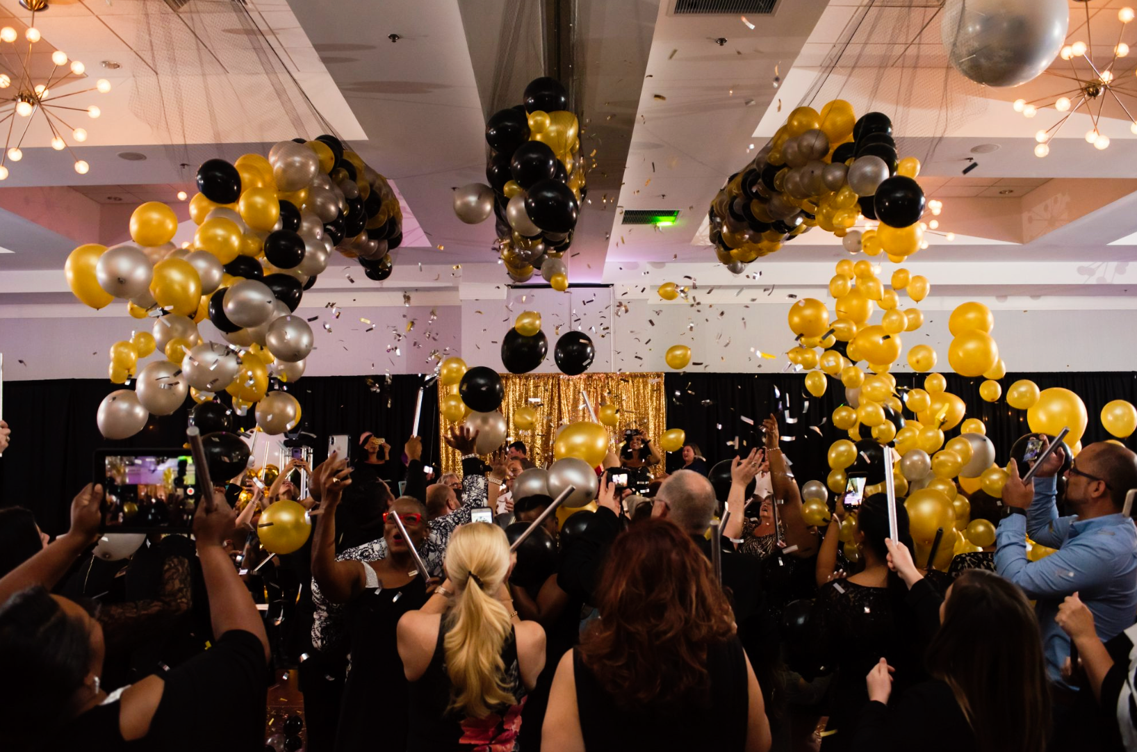 A crowd of people are standing in a room with balloons and confetti.