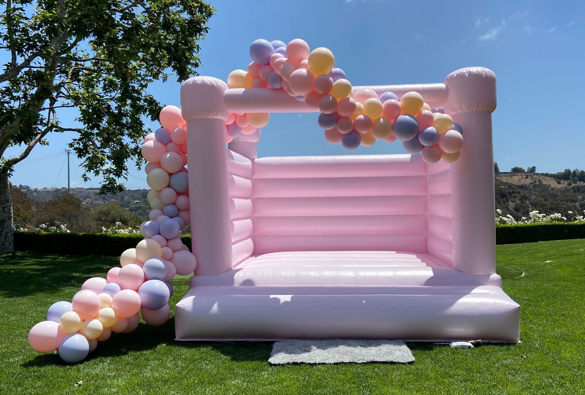 A pink bouncy castle decorated with balloons is sitting on top of a lush green field.