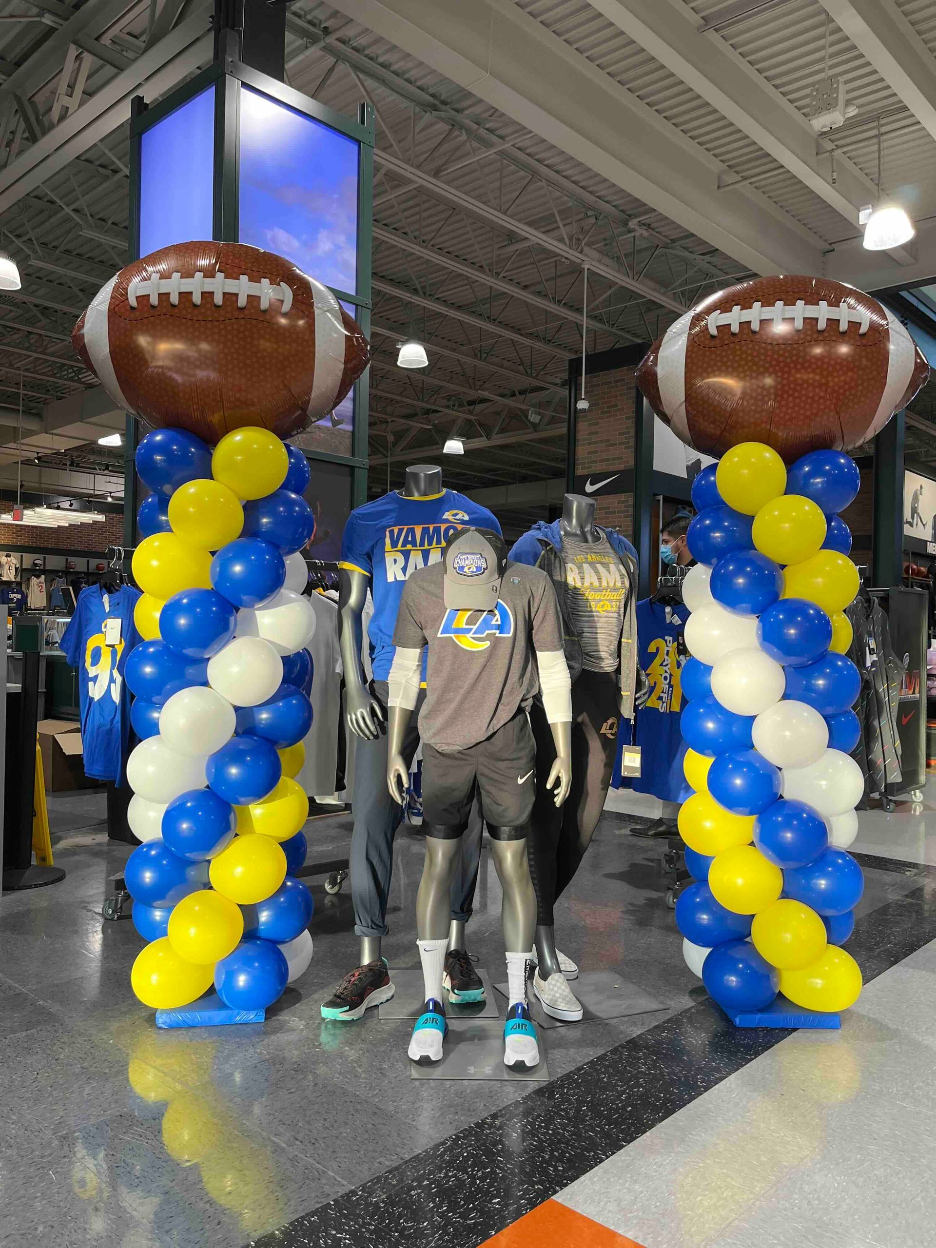 A store is decorated with blue and yellow balloons and footballs. Balloon columns for retail stores.