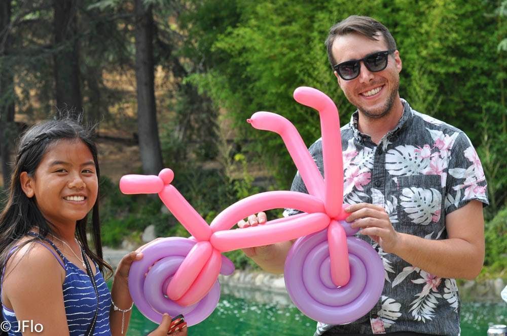 A man and a girl are holding a pink and purple balloon bike.