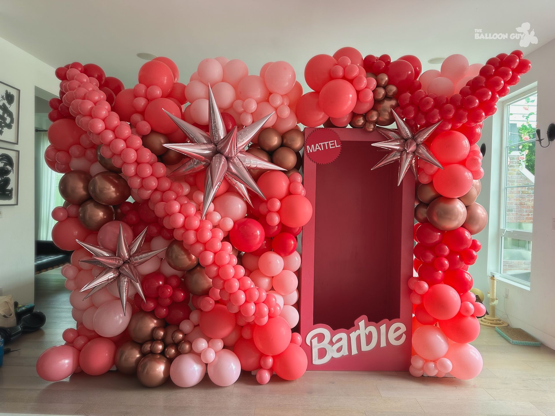 A wall of pink and red balloons with a barbie sign in the middle.