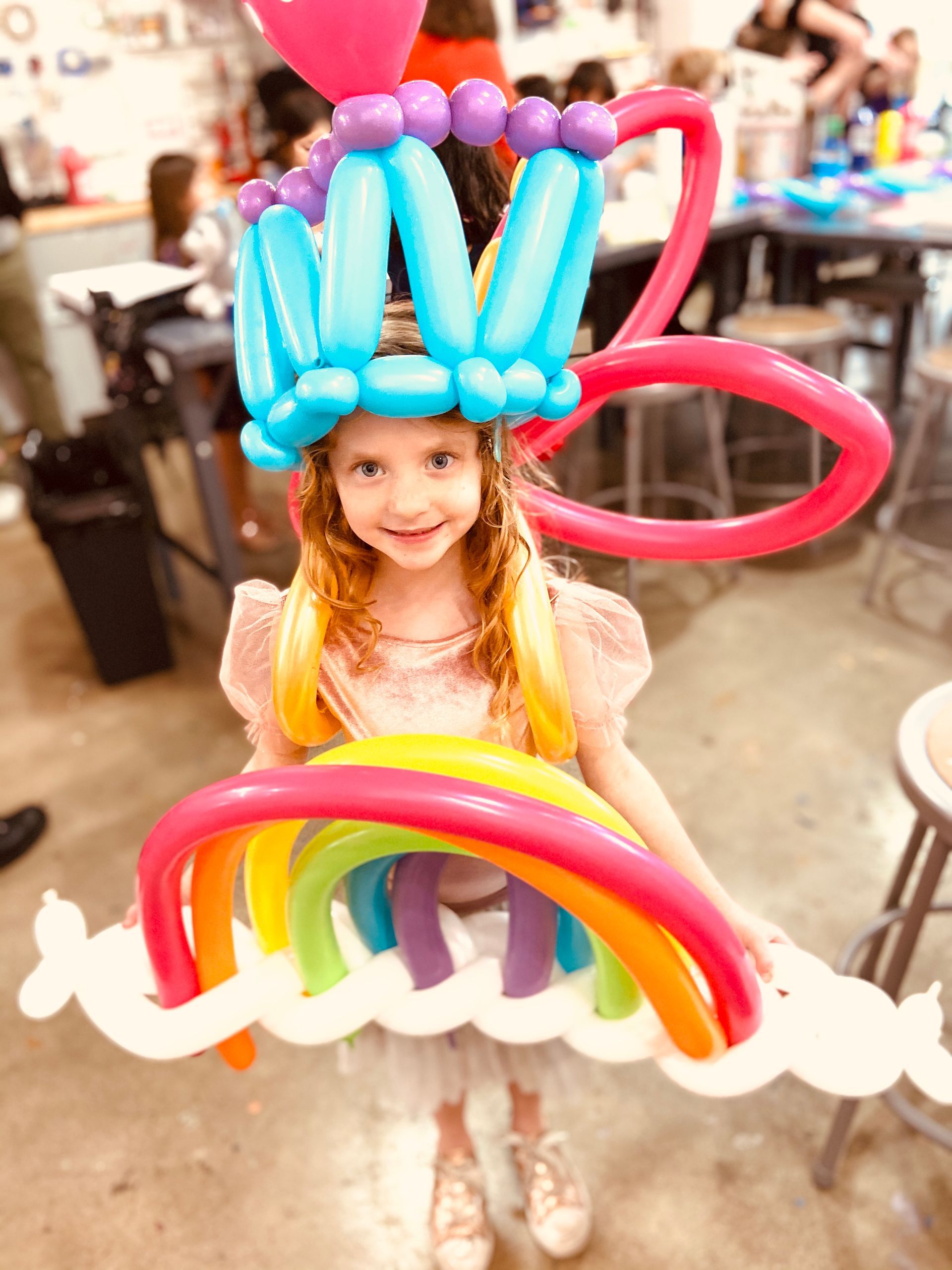 A little girl is wearing a hat made out of balloons.
