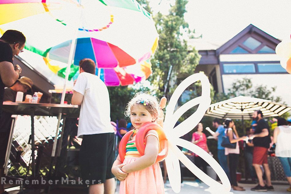 A little girl wearing a fairy costume is standing in front of a colorful umbrella