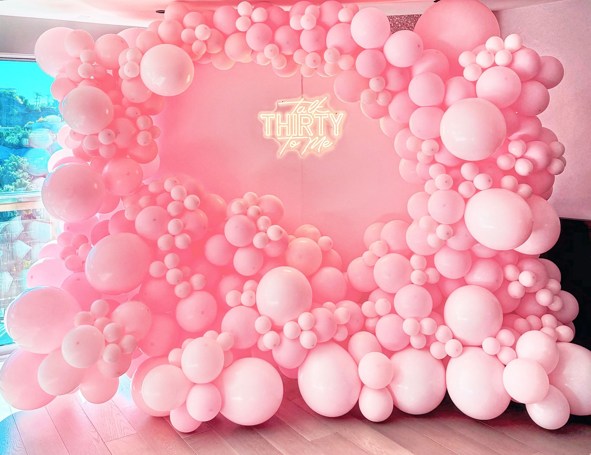 A wall filled with pink balloons and a neon sign.