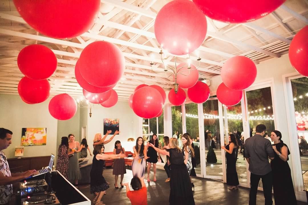 A group of people are dancing in a room with red balloons hanging from the ceiling.