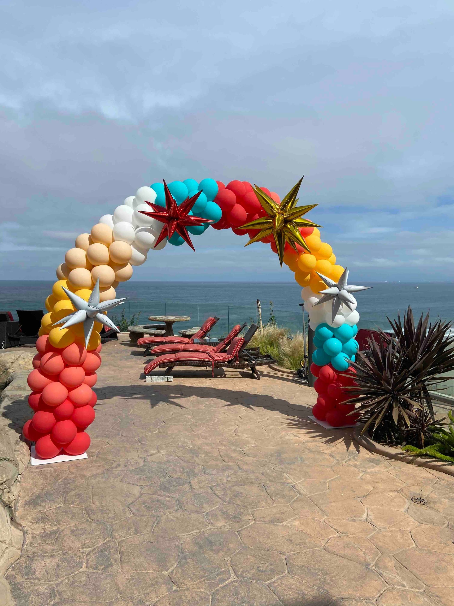 A colorful balloon arch is sitting on a patio overlooking the ocean.