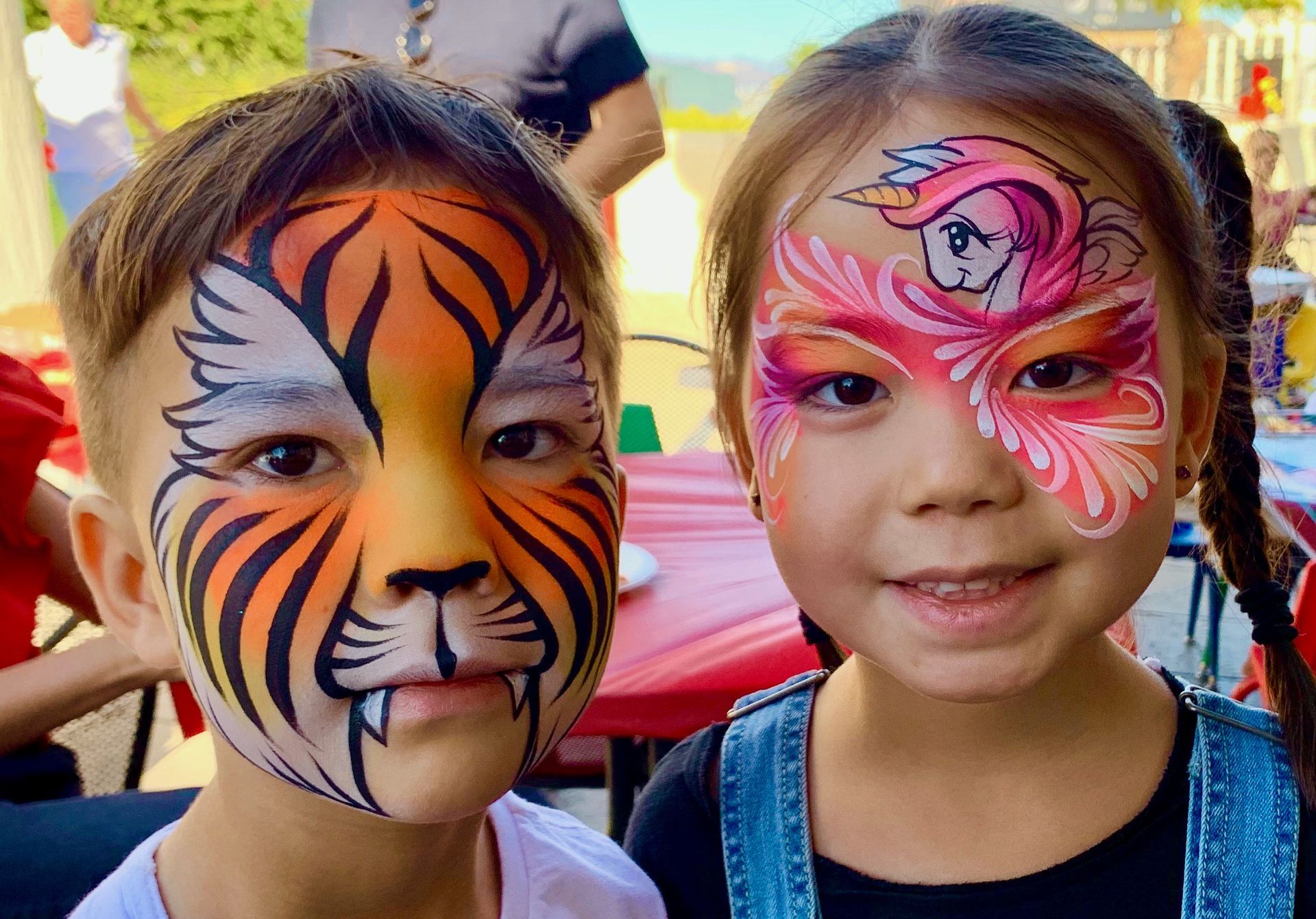 A boy and a girl with their faces painted like a tiger and a unicorn.
