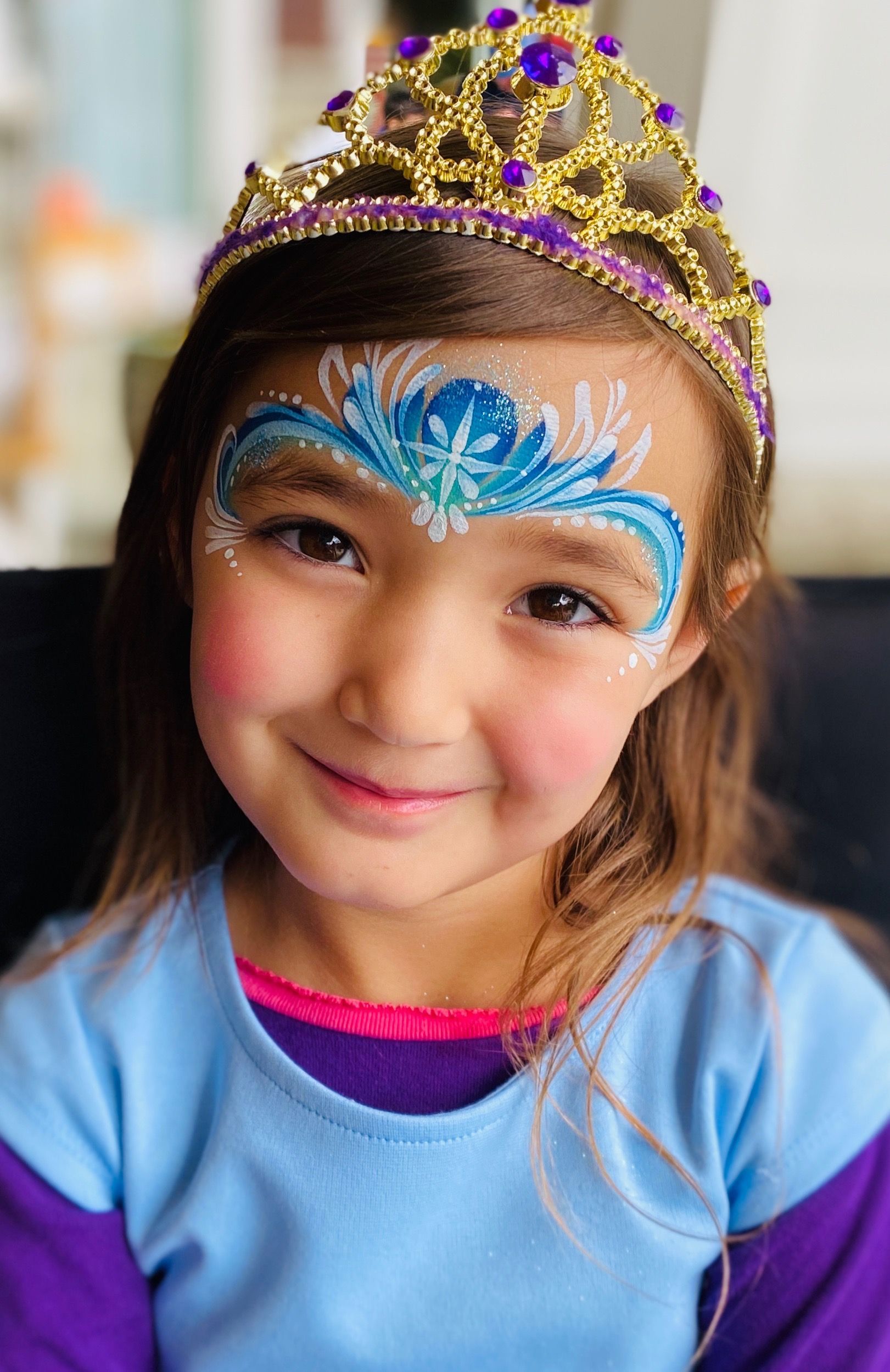 A little girl with face paint and a tiara on her head.