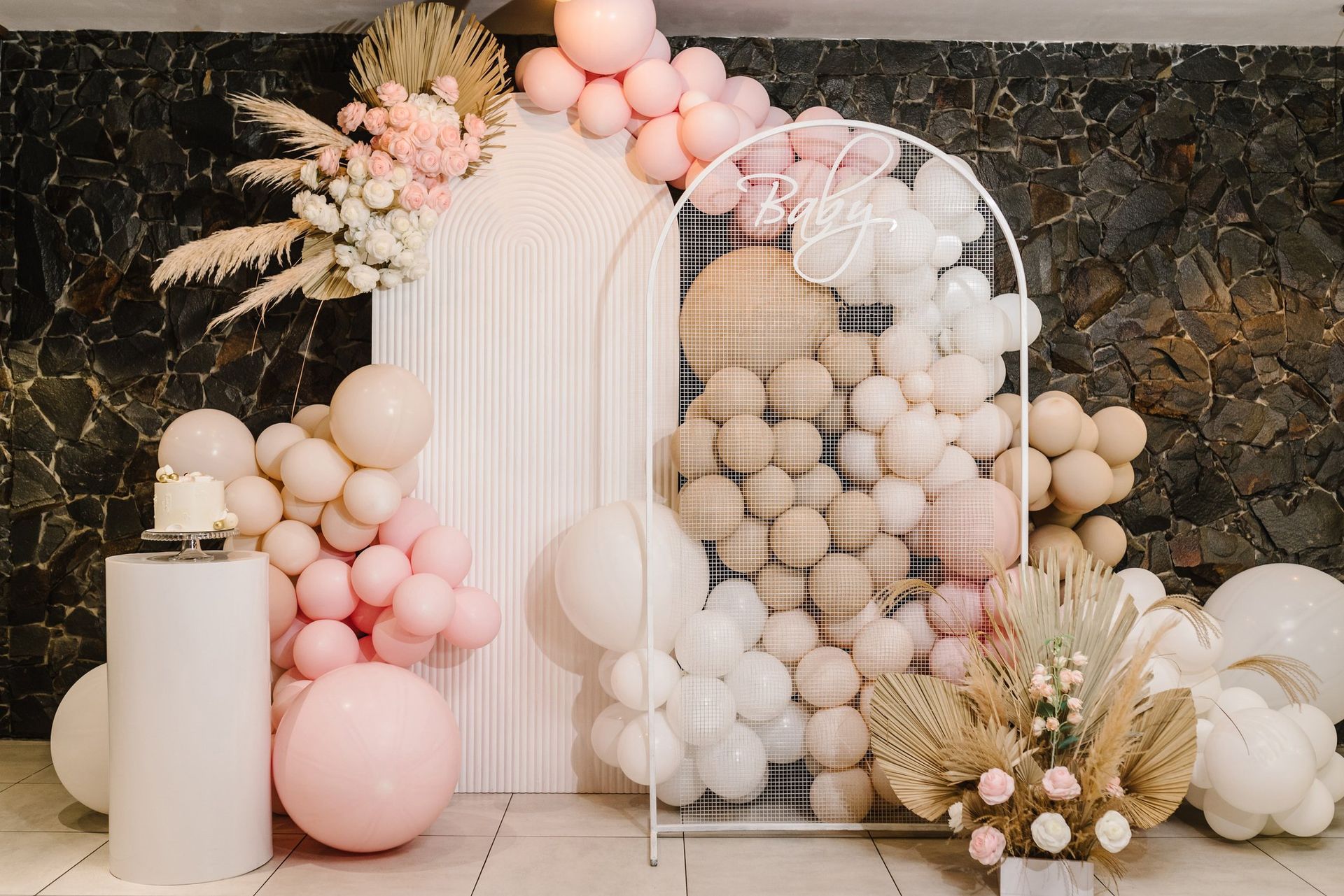 A wall filled with pink and white balloons and flowers.