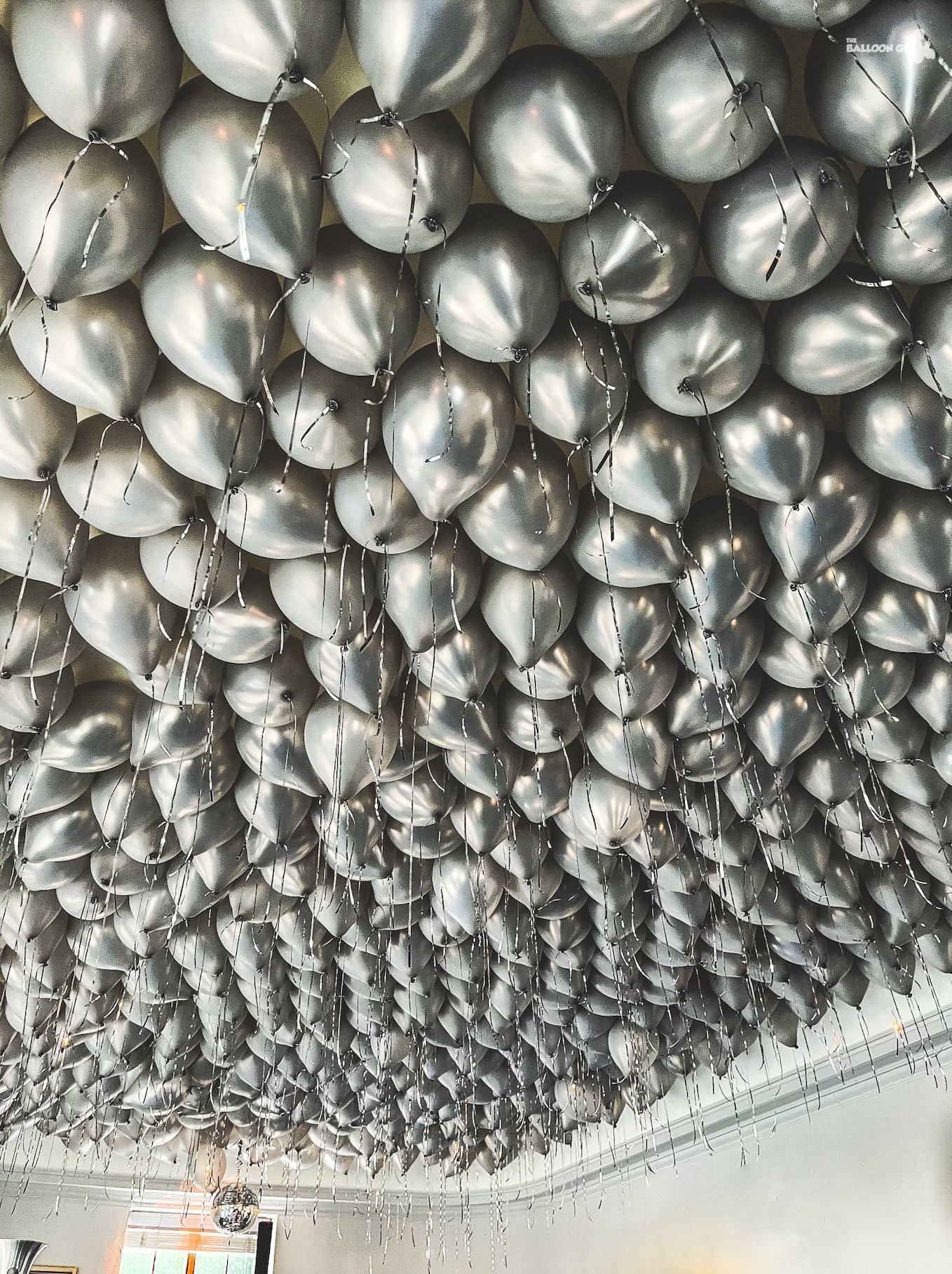 A bunch of silver balloons are hanging from the ceiling.
