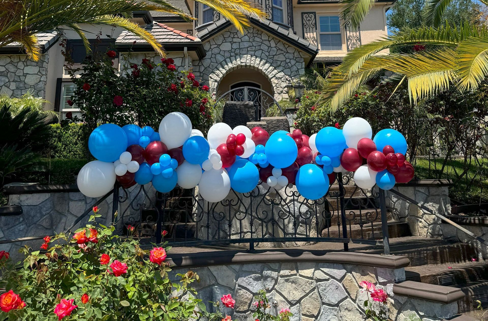 A bunch of balloons are hanging from a fence in front of a house.