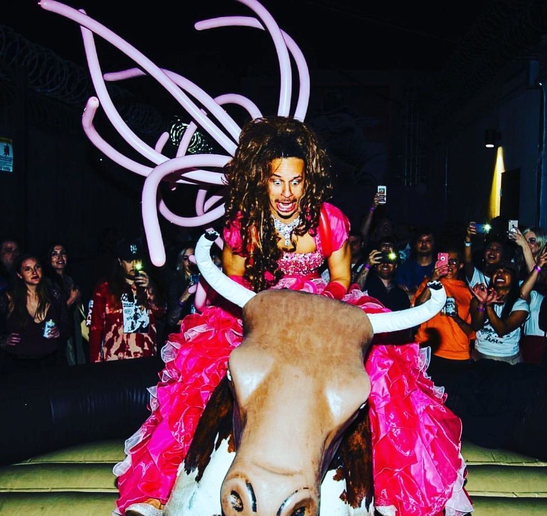 A man in a pink dress is riding a bull