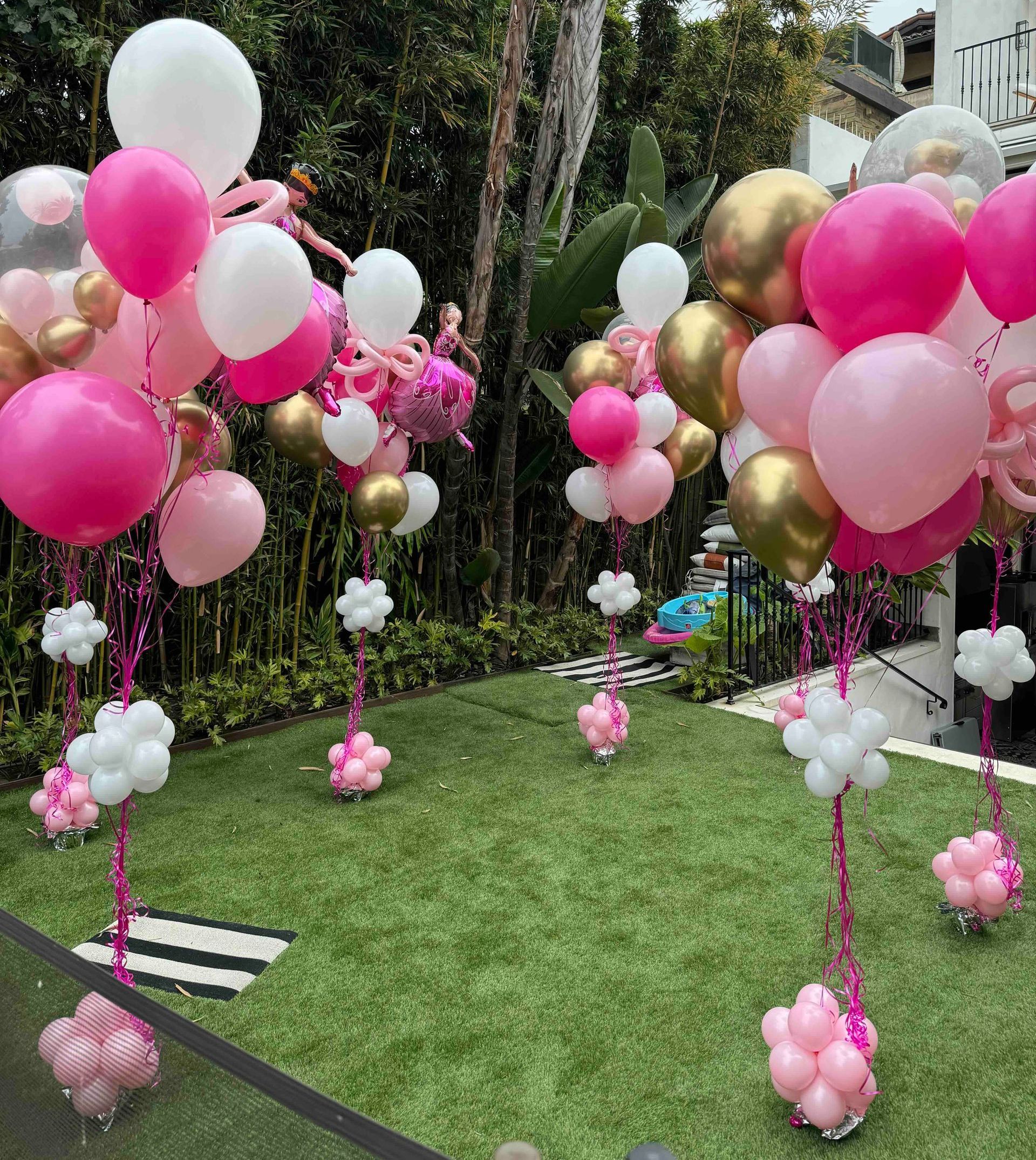 A bunch of pink and gold balloons are sitting on top of a lush green field.