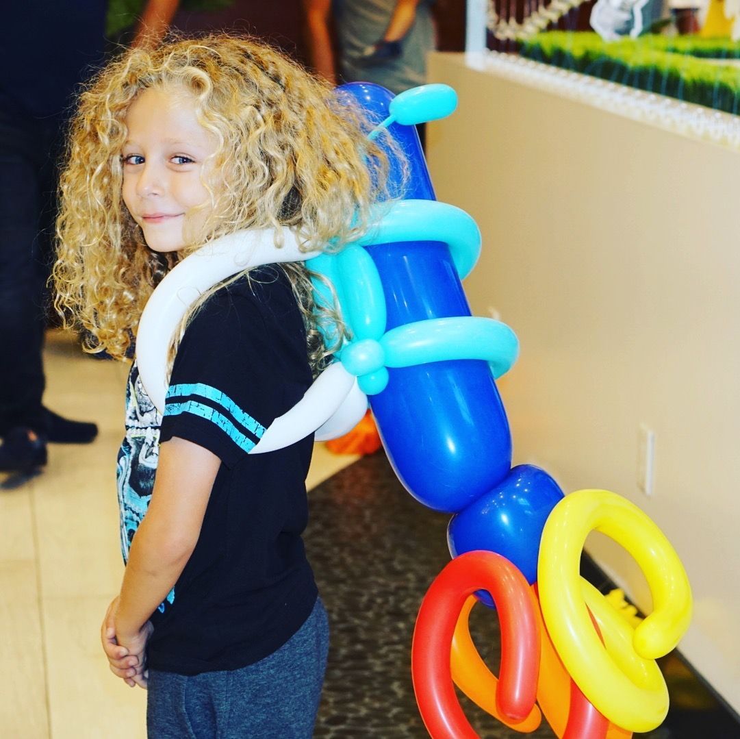 A child with curly hair is wearing balloons on their back