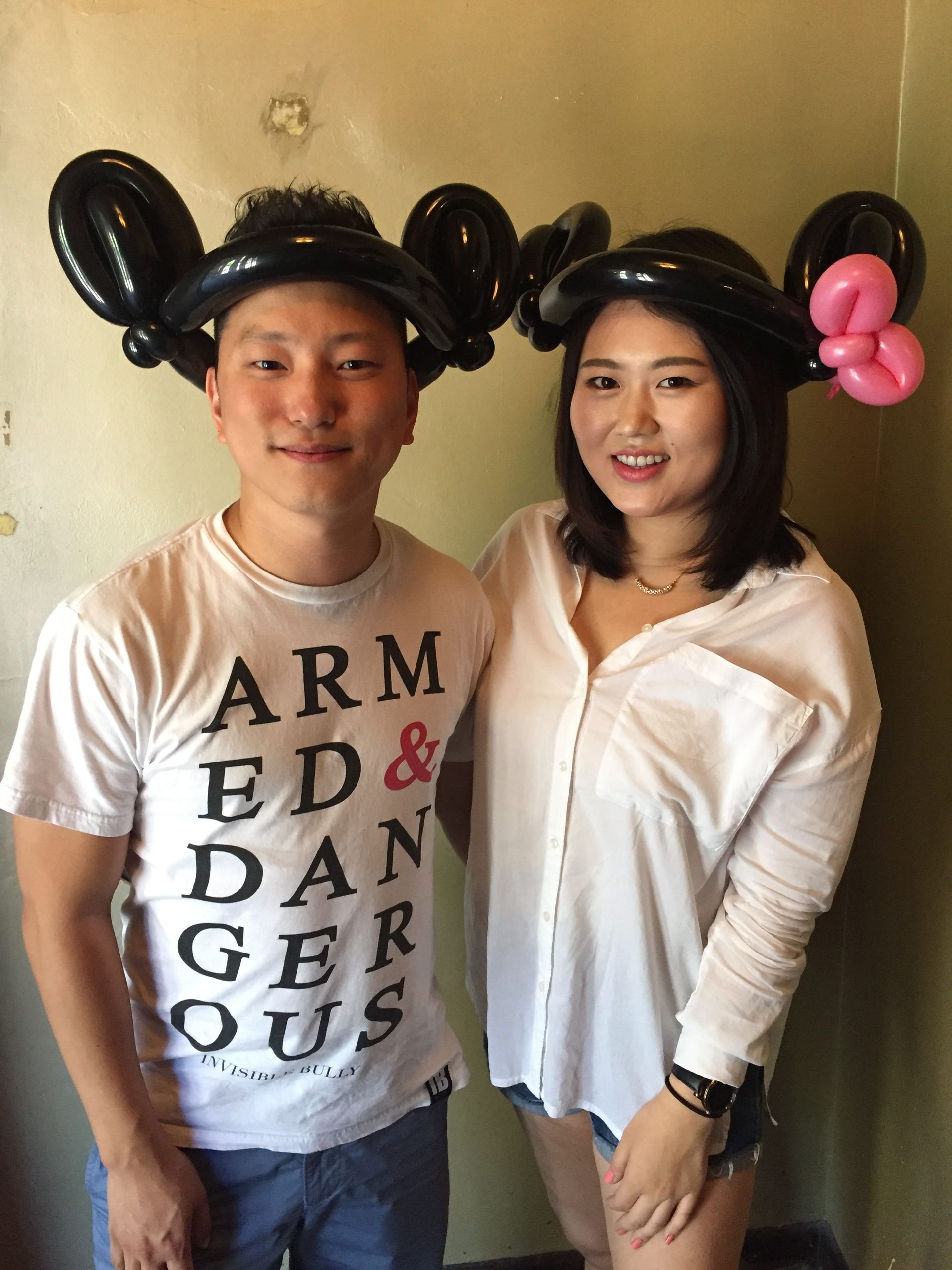A man and a woman are posing for a picture with mickey and minnie mouse balloons on their heads