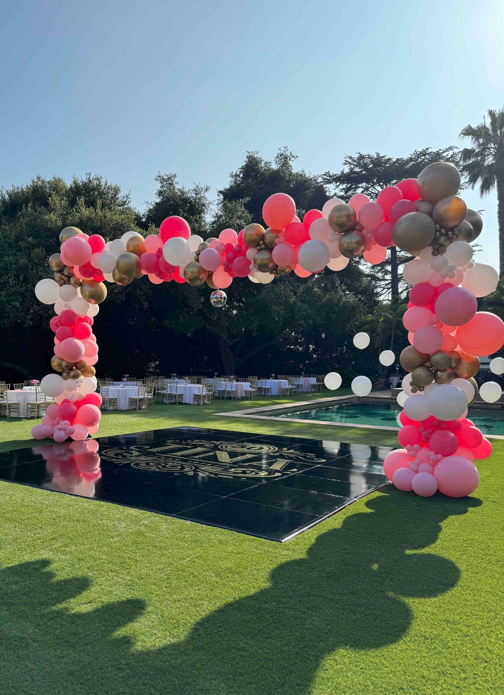 A bunch of pink and gold balloons are sitting on top of a black dance floor.