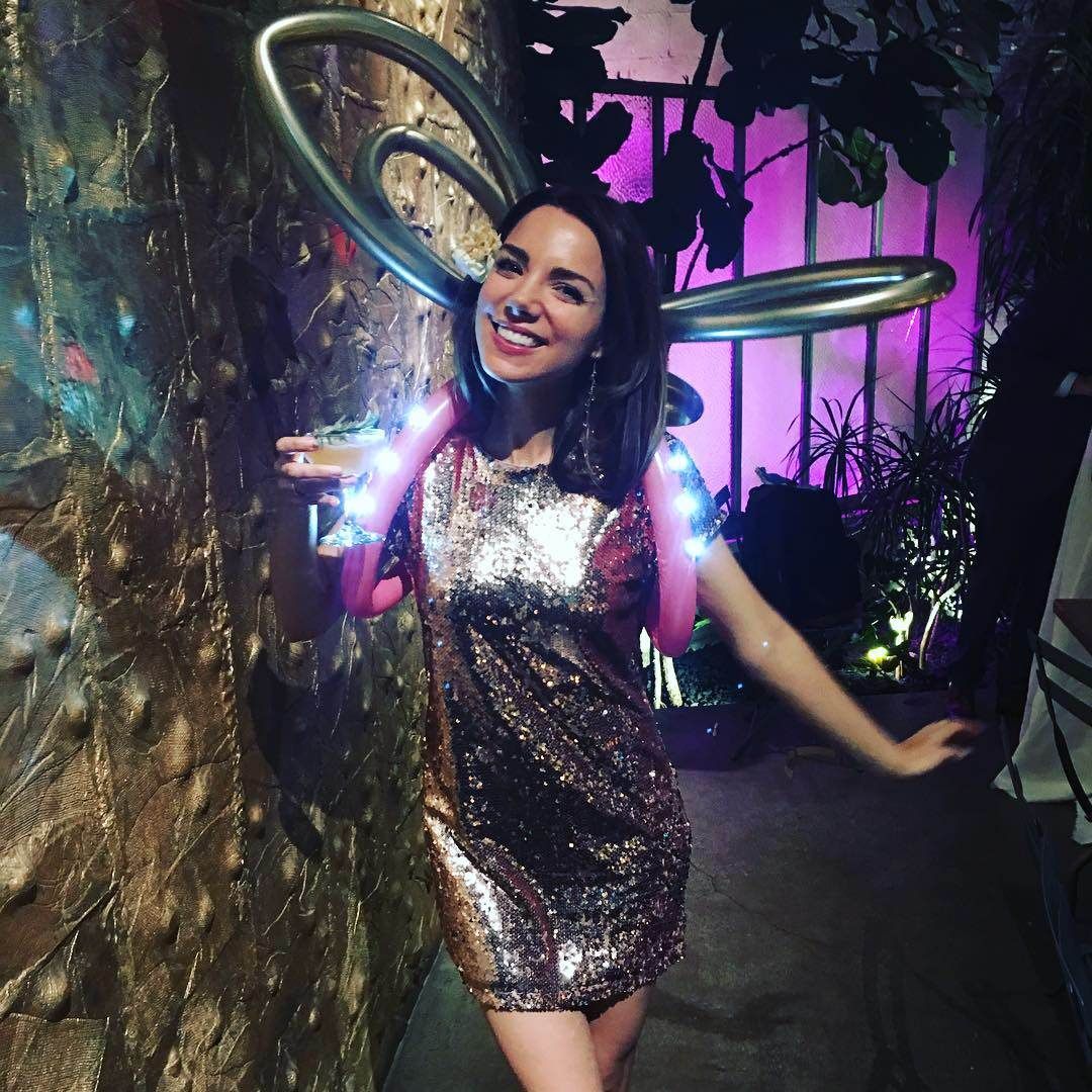 A woman in a sequined dress is standing in front of a purple wall.