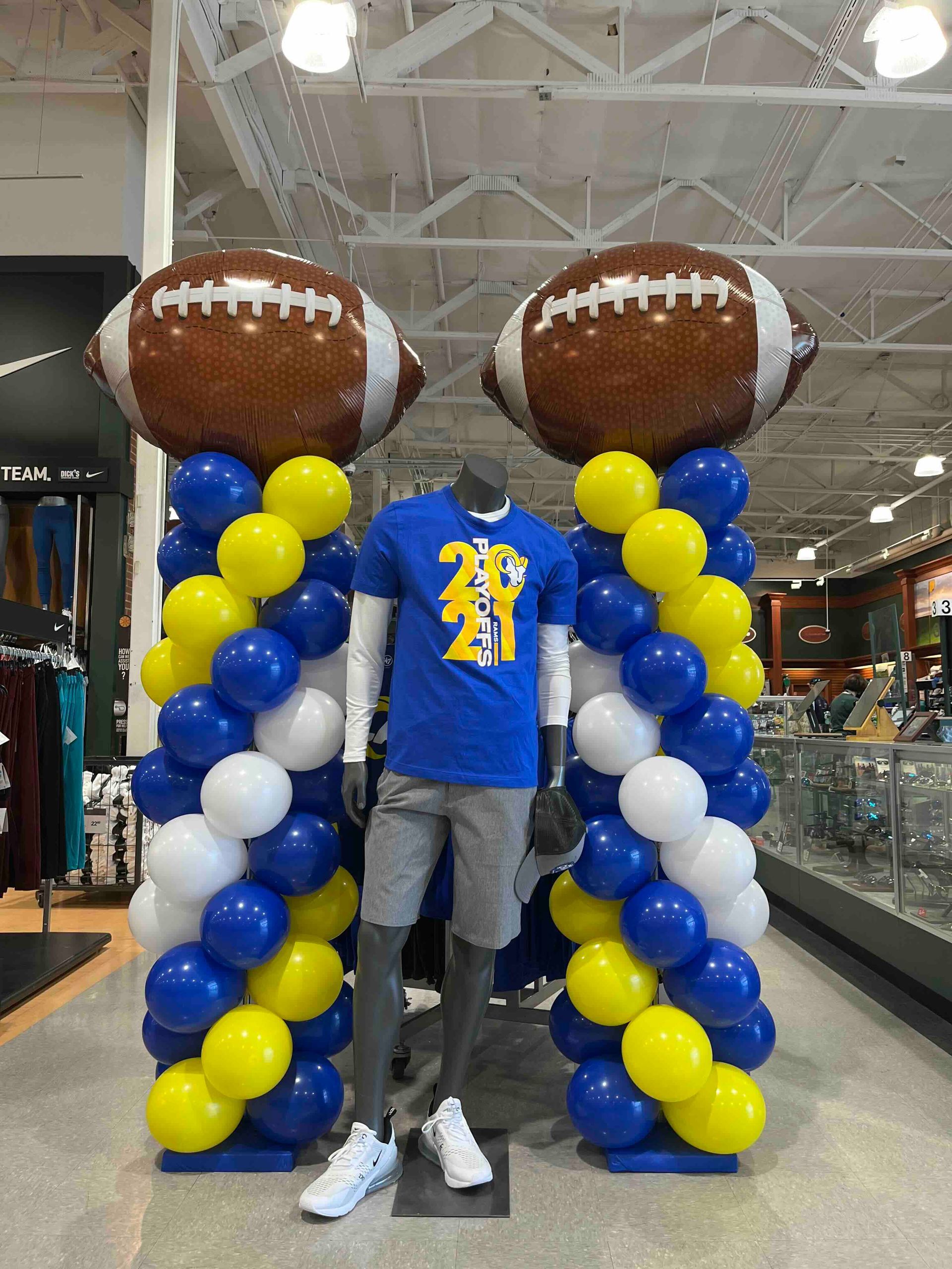 Two mannequins are standing next to balloons in a store.