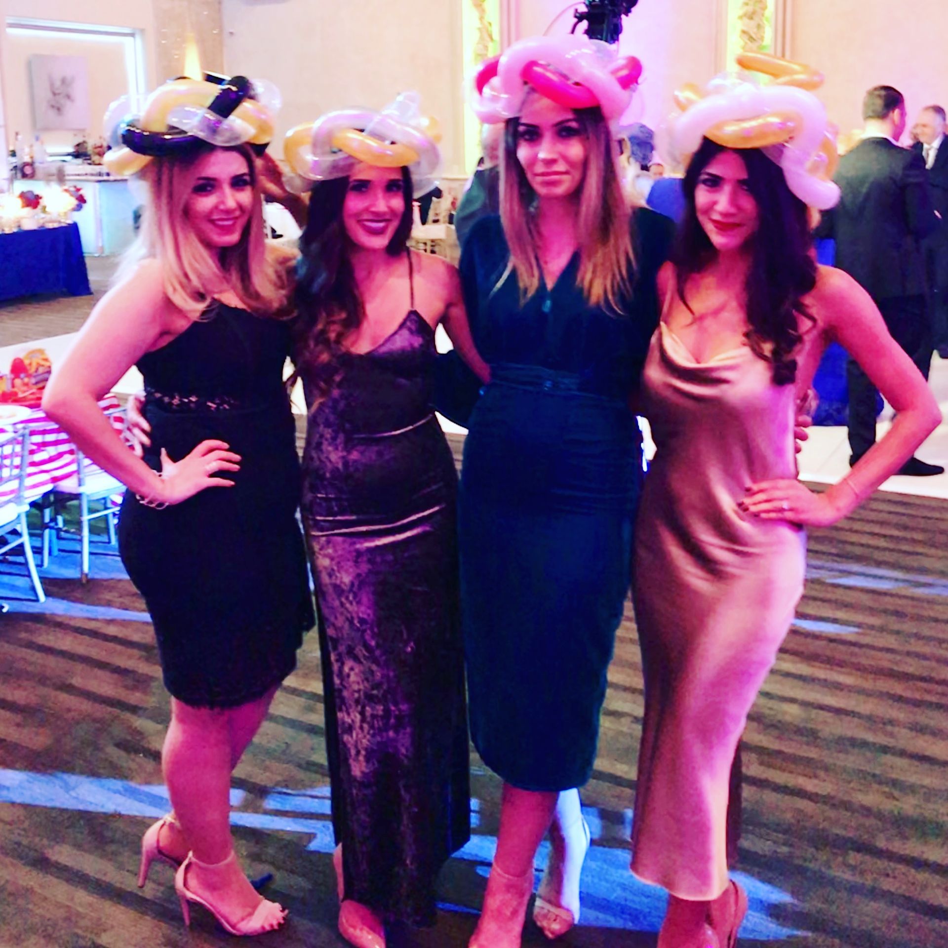 Four women posing for a picture with balloon hats on their heads