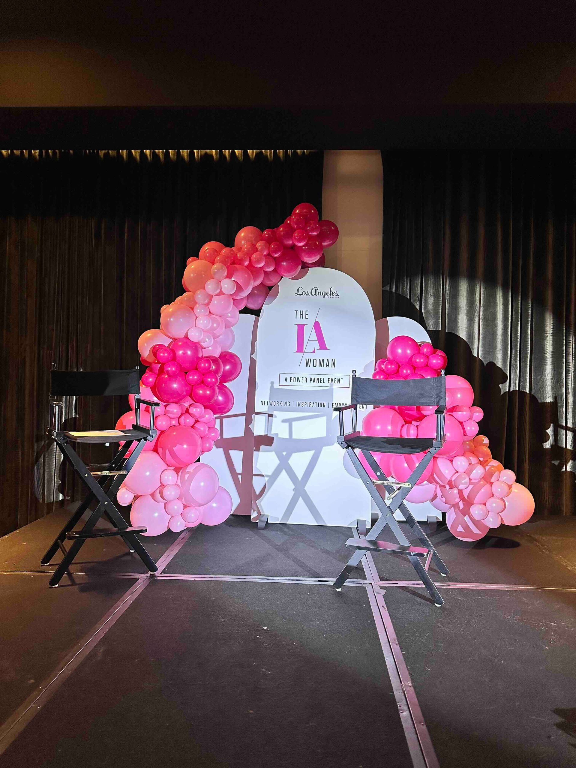 Two chairs are sitting on a stage decorated with pink balloons.