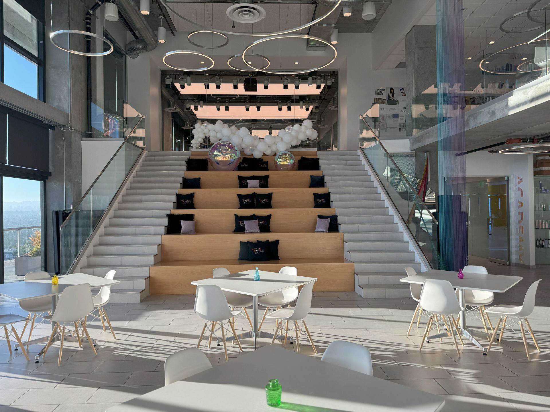 A large room with tables and chairs and stairs in the middle.