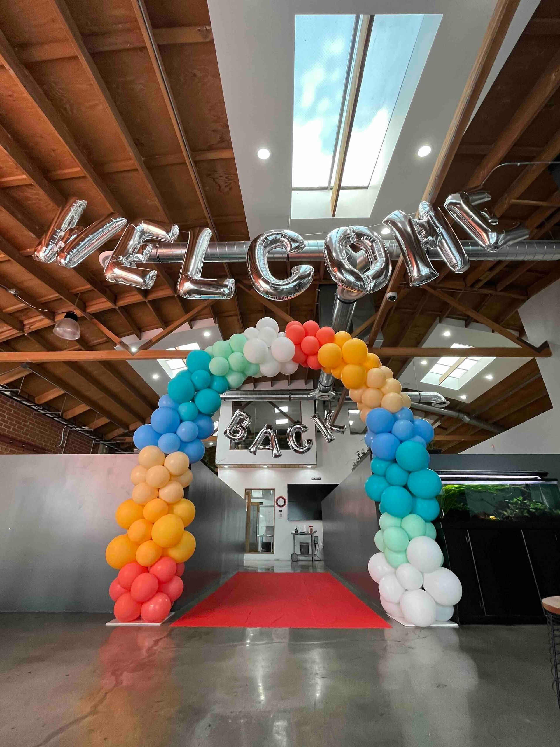 A balloon arch with the word welcome written on it. Arch for welcome back to the office.
