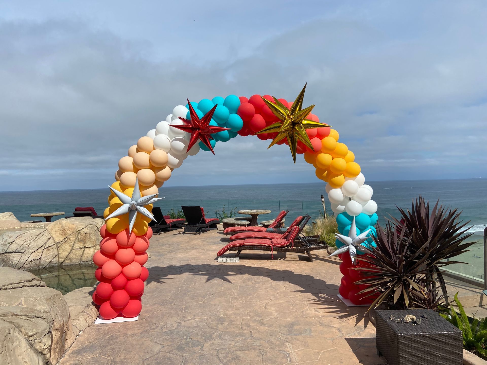 A colorful arch made of balloons and starfish on a patio overlooking the ocean.